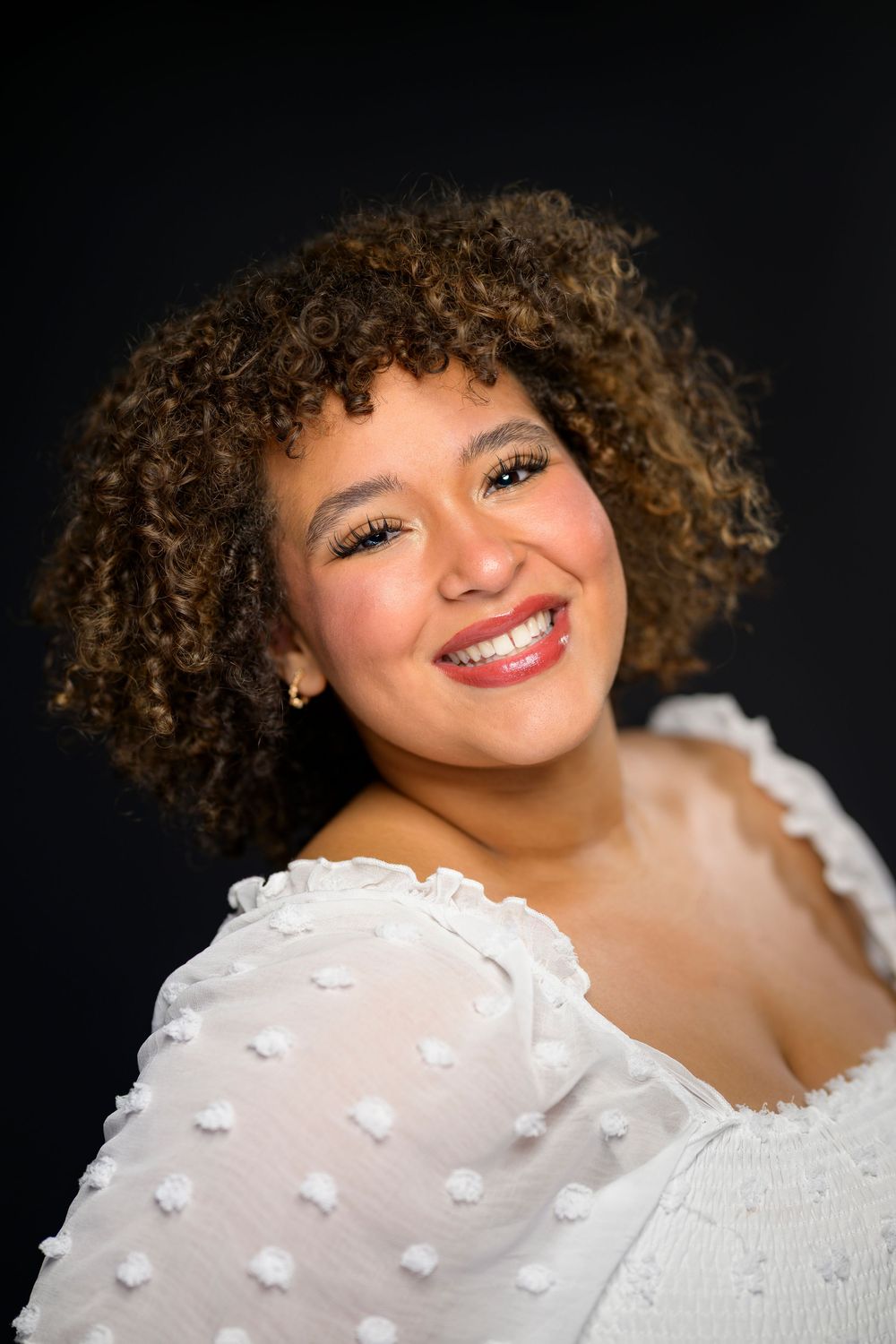 Close-up portrait of a young woman with curly hair and bold red lips against dark background.