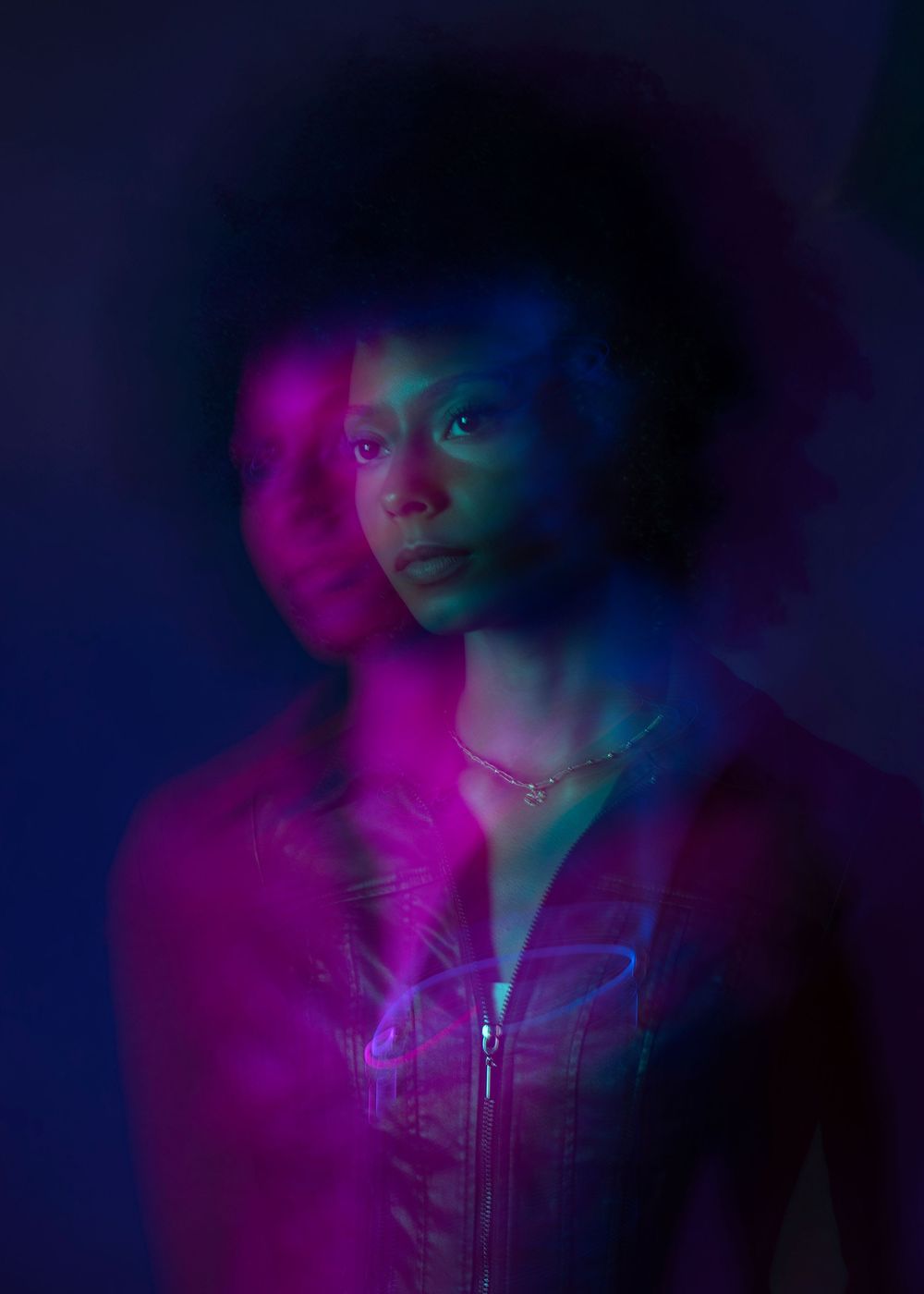 Artistic double-exposure portrait of young Black woman with afro under vibrant pink and blue neon lighting.