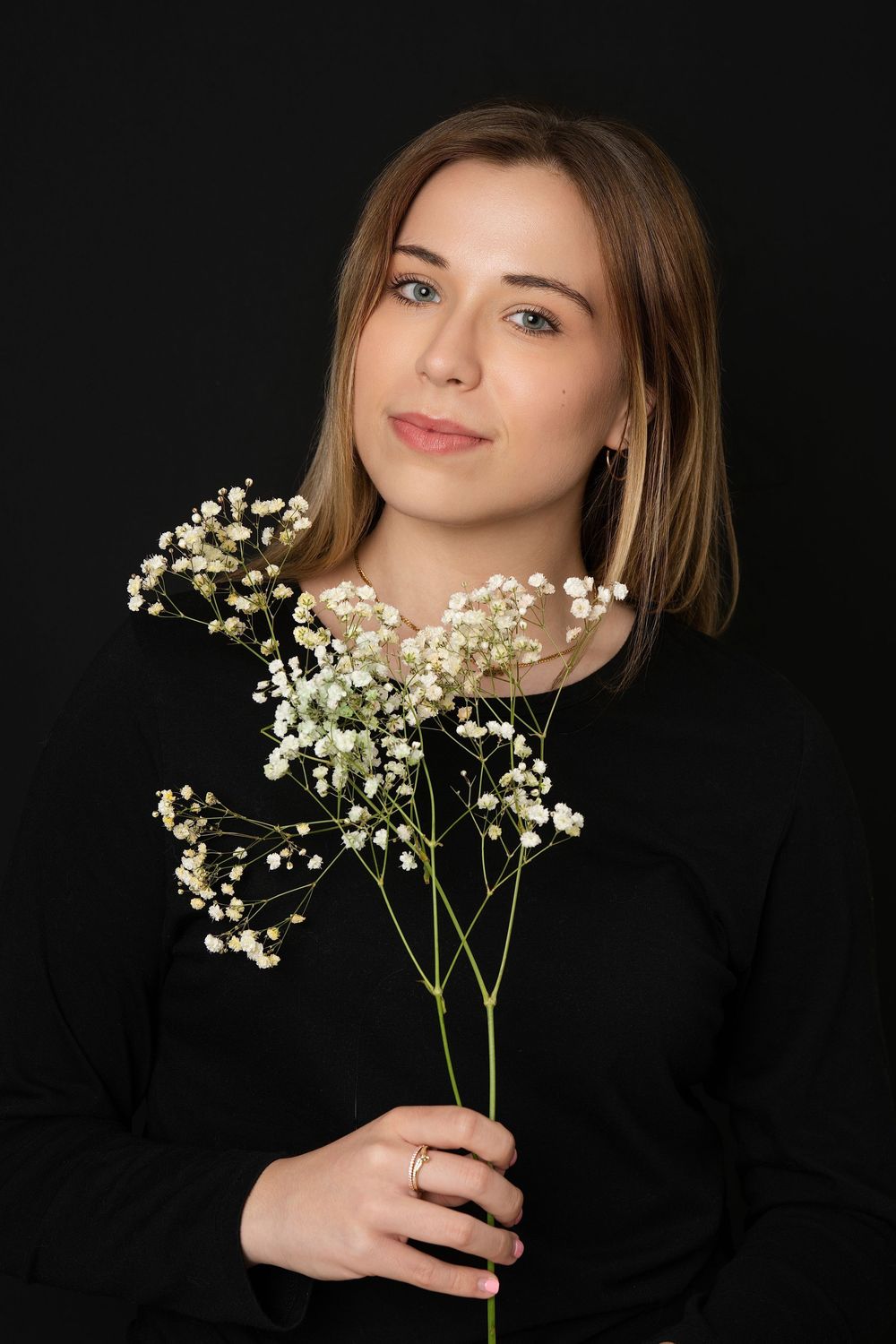 Young blonde woman holding delicate white gypsophila flowers against a dark black studio background.