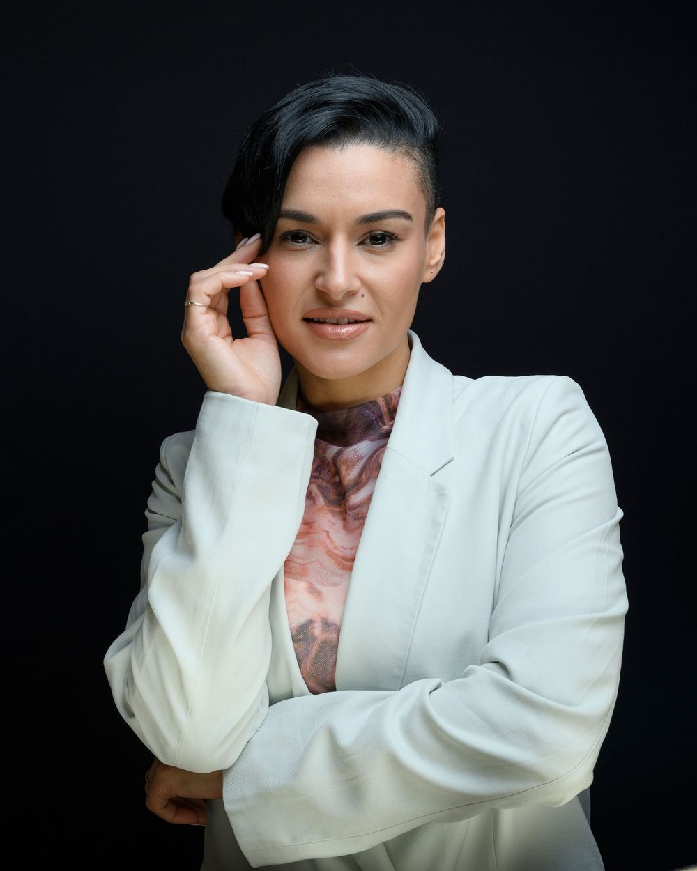 Professional woman in white blazer posing confidently against dark background.