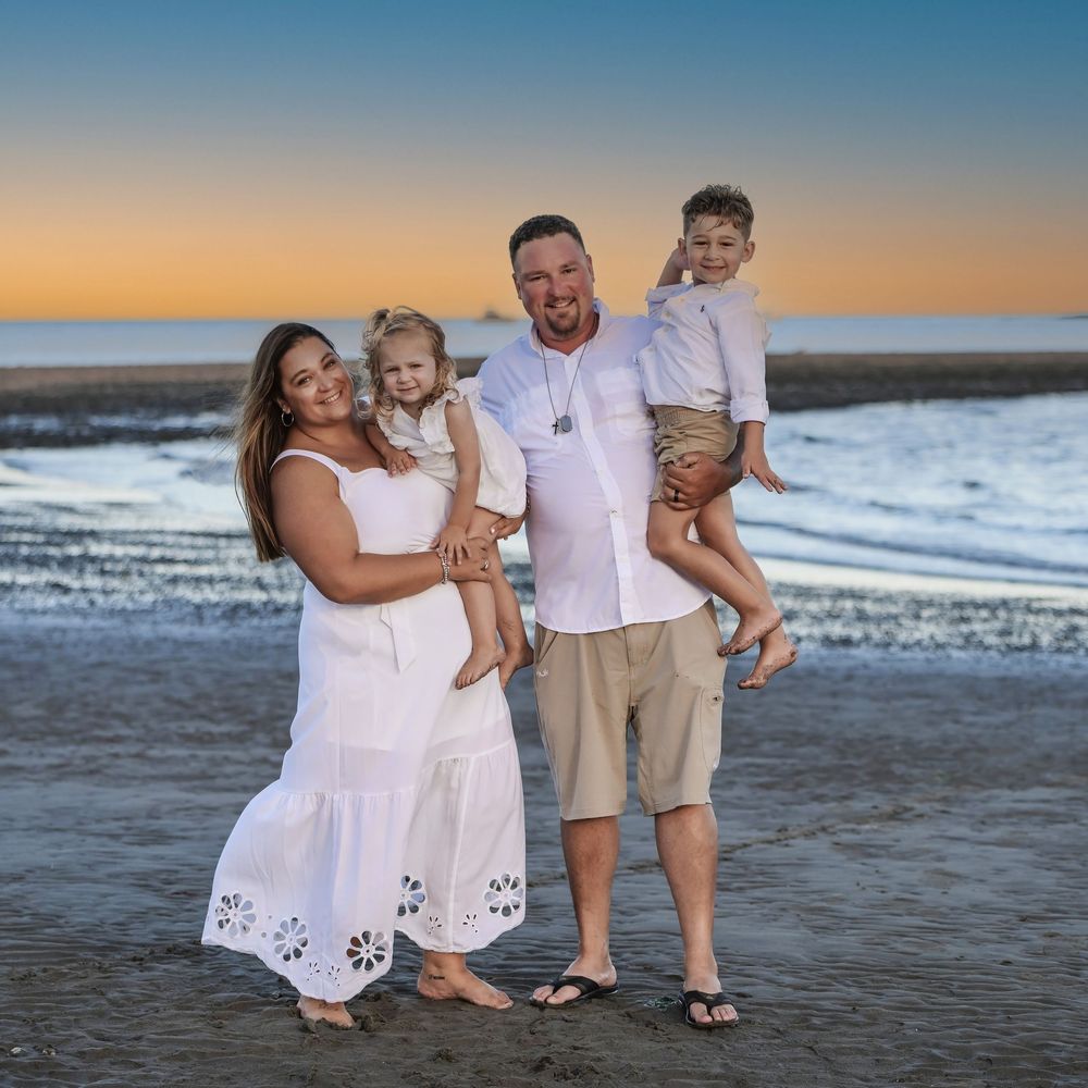 A portrait of a family wearing white and standing on a beach