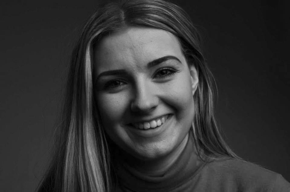Black and white portrait of a smiling woman with long blonde hair against dark background.