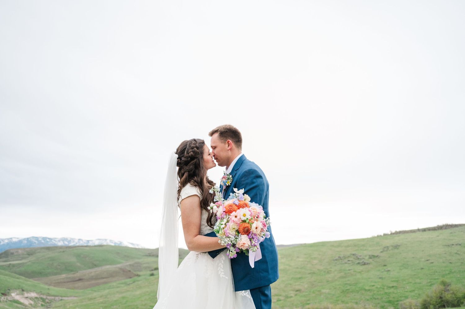 Romantic wedding portrait with colorful bouquet against overcast sky.