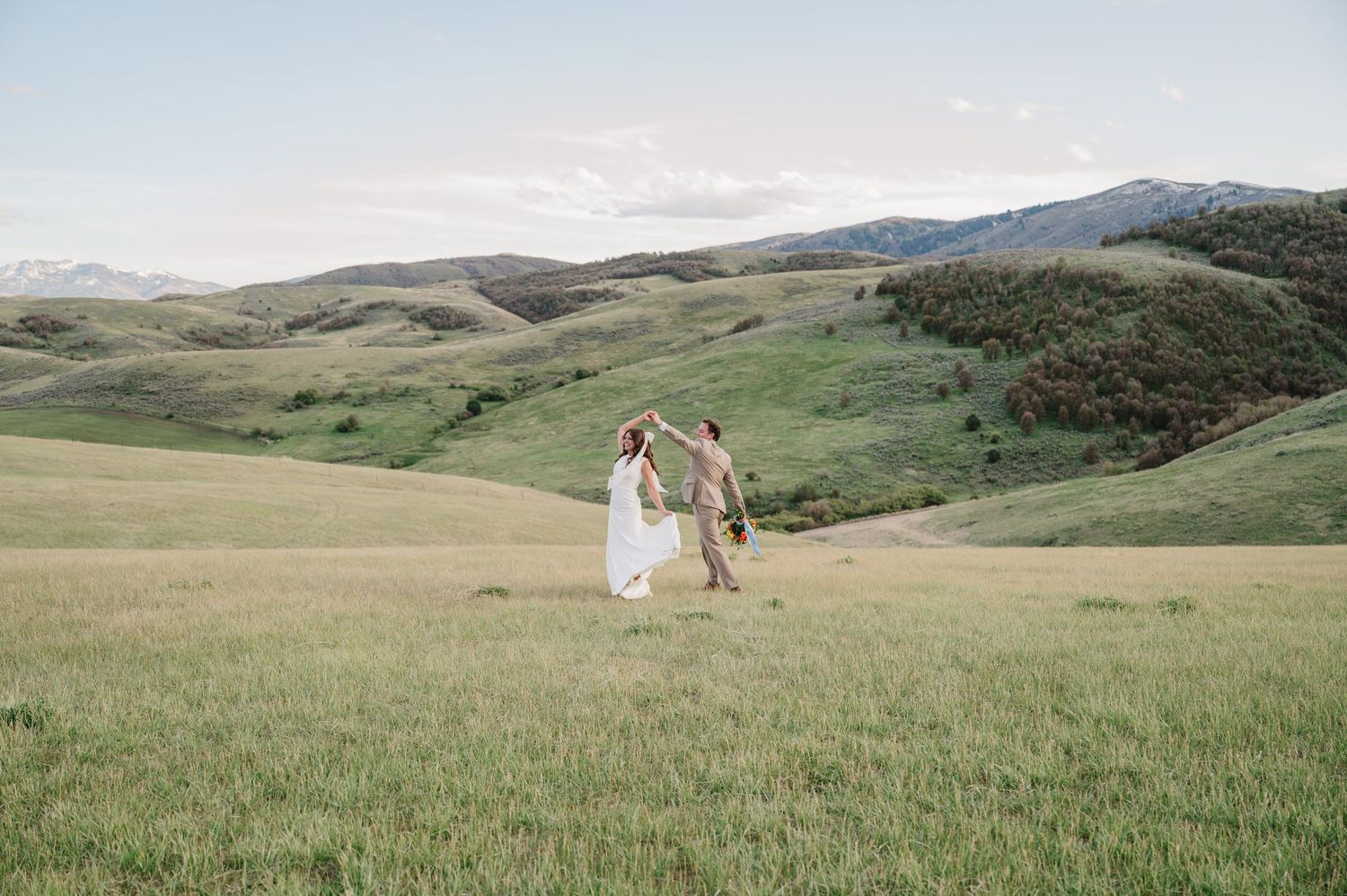 Couple dancing in a lush green meadow with rolling hills and mountains in the background during a wedding shoot.