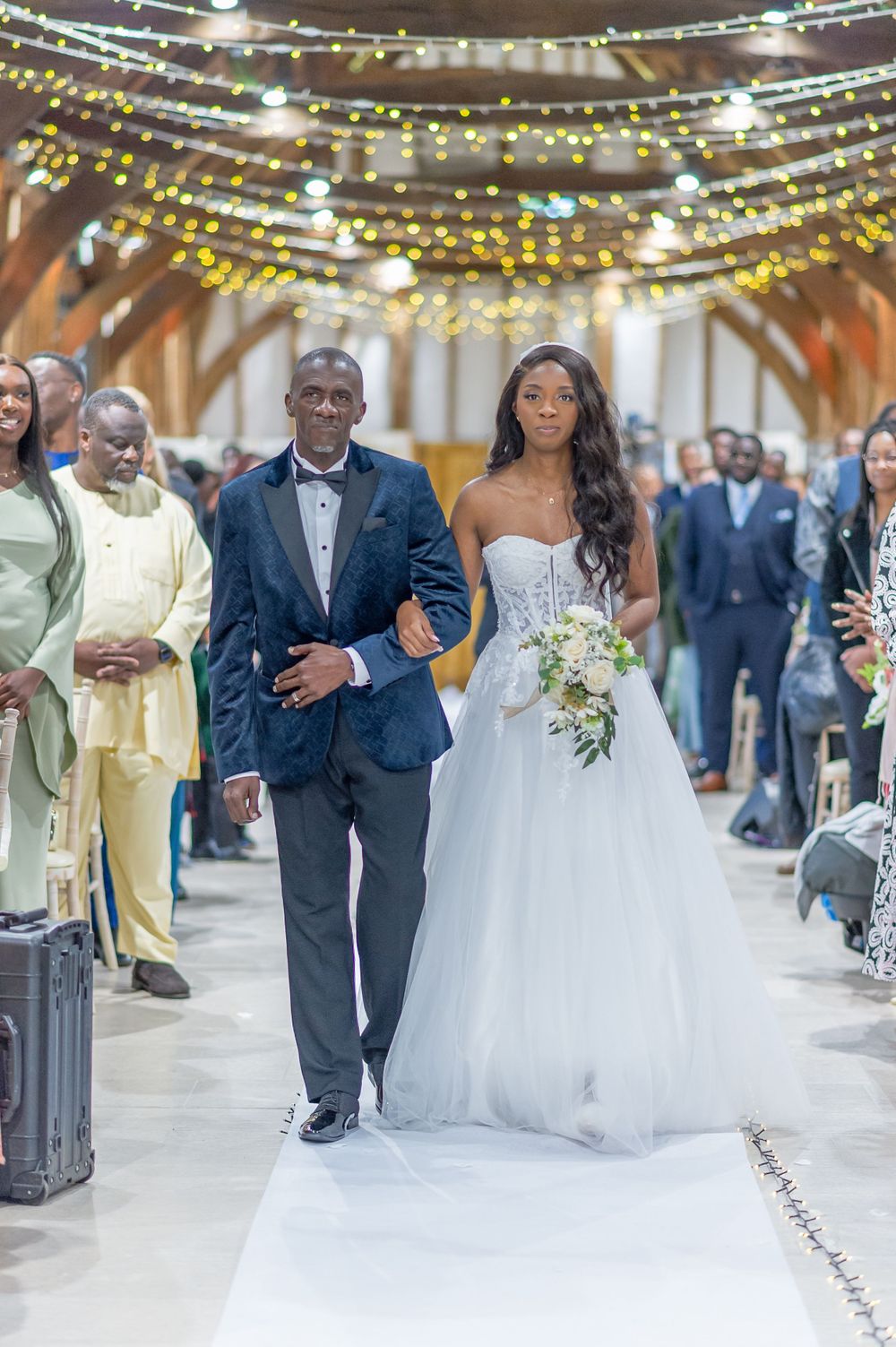 A couple walking down the aisle under strings of twinkling lights at their wedding ceremony.