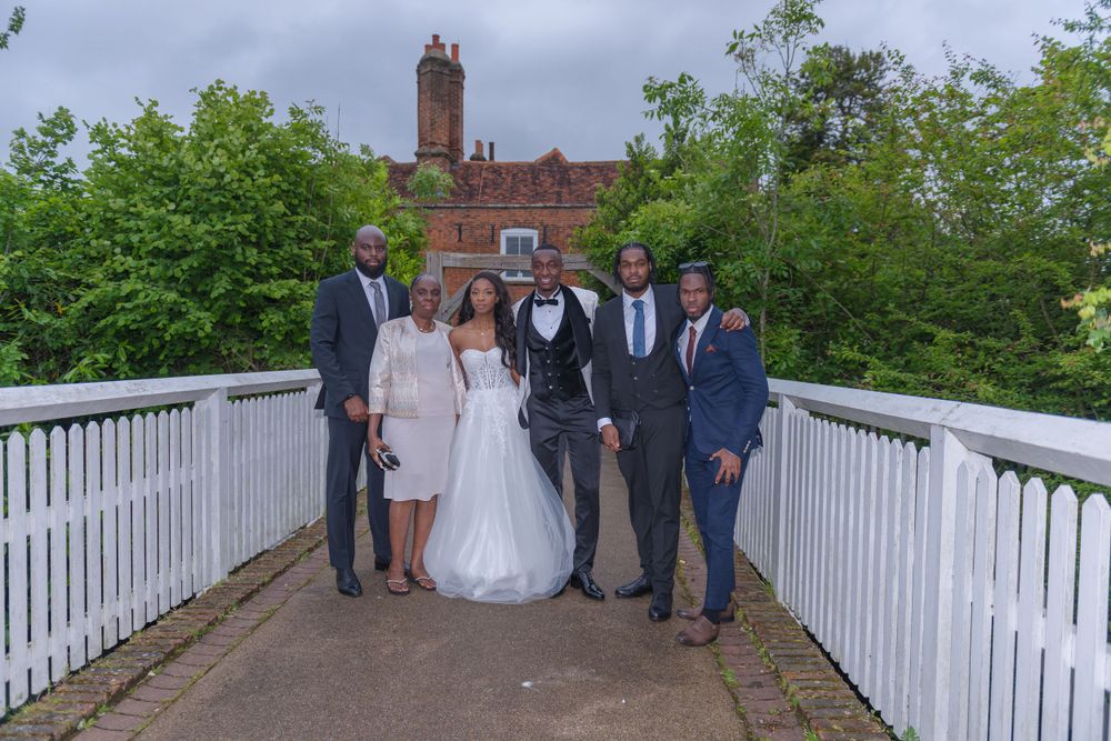 Wedding party gathered on white wooden bridge for outdoor photo session.