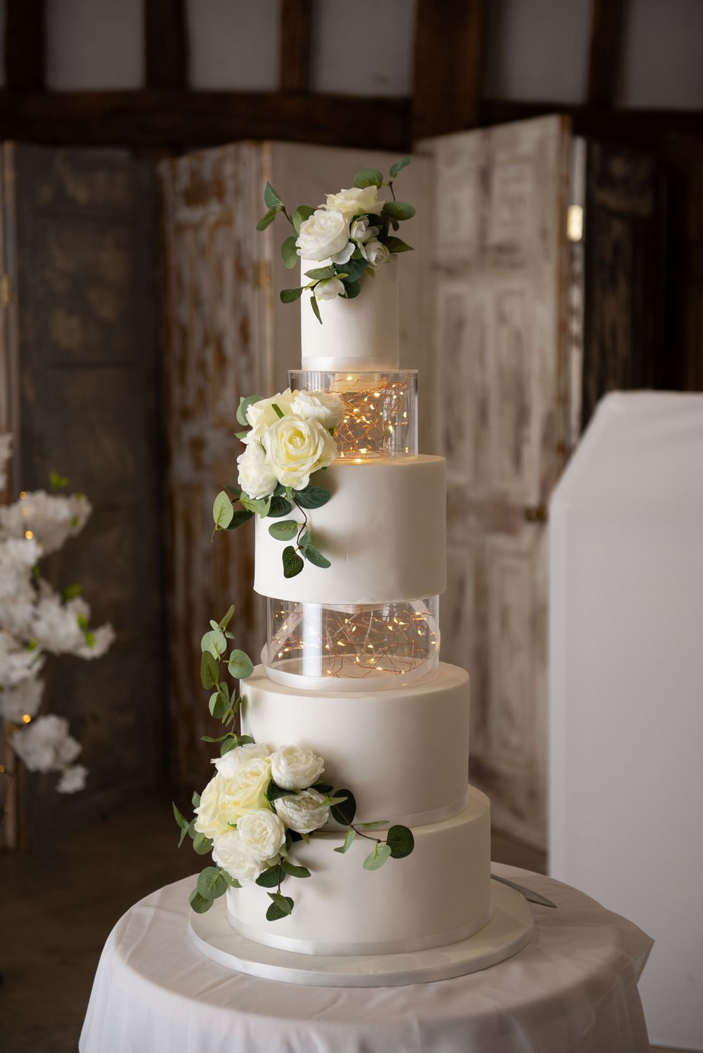 Elegant five-tier white wedding cake decorated with metallic accents and fresh white roses.
