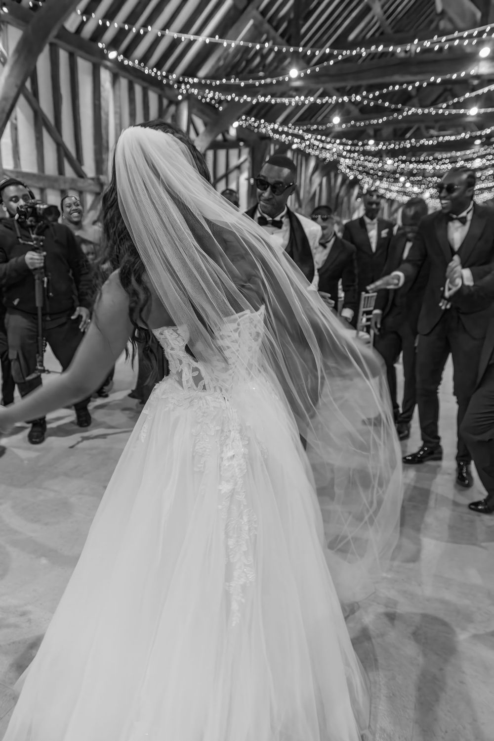 Black and white photo of a bride dancing under twinkling reception lights.