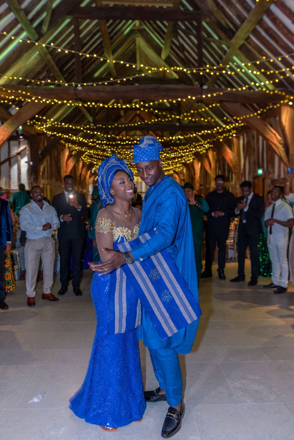 Wedding reception in rustic barn with string lights and dancers in bright blue traditional outfits.