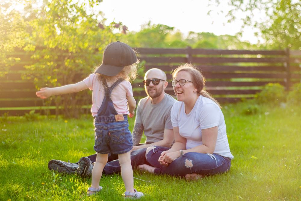 People sitting on grass in backyard enjoying sunny afternoon while child plays at sunset.