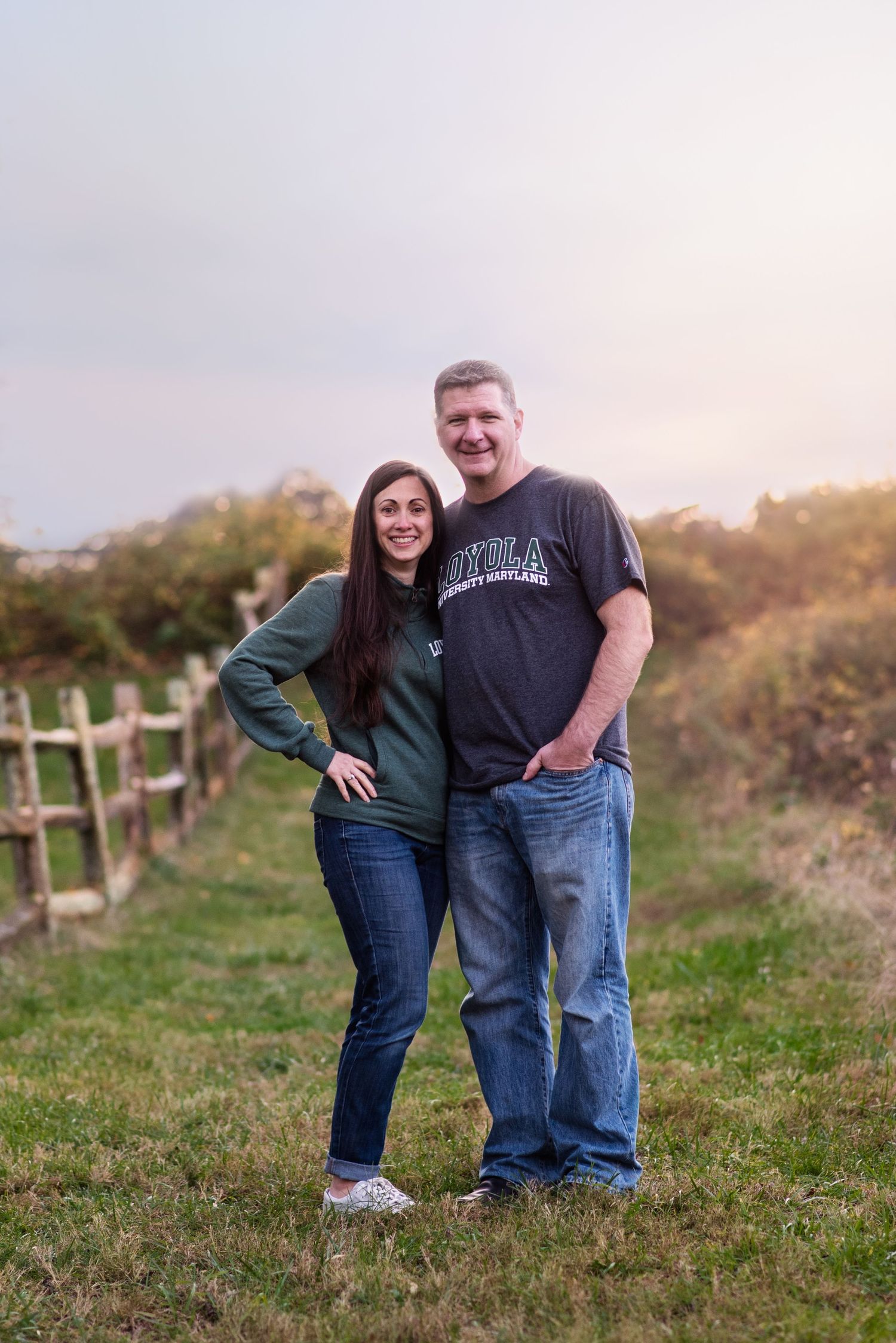 Casual couple photo on grassy hillside with fence and sunset lighting in Monmouth County NJ