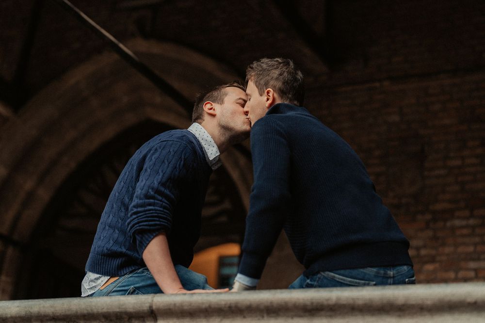 Two people share an intimate moment while sitting on stone steps beneath an archway.