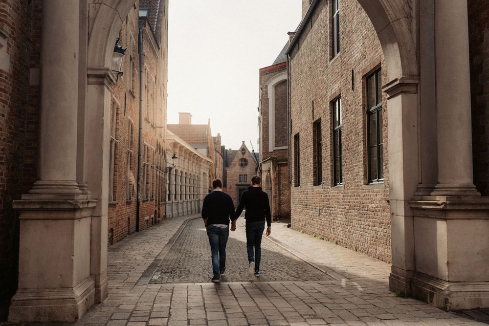 Two figures walk down a narrow historic street lined with traditional architecture.