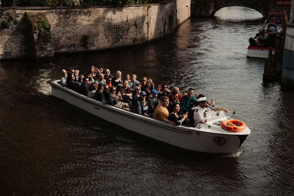 Tourist boat filled with passengers cruising through a historic canal in Bruges.