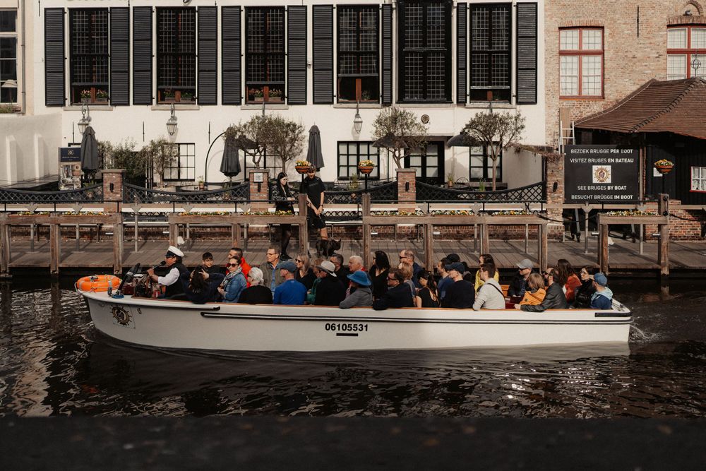 Crowded sightseeing boat navigating through the canals of Bruges.