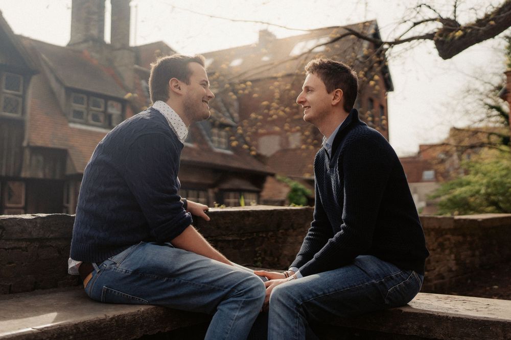 Two people share an intimate conversation while sitting on a stone wall at sunset.
