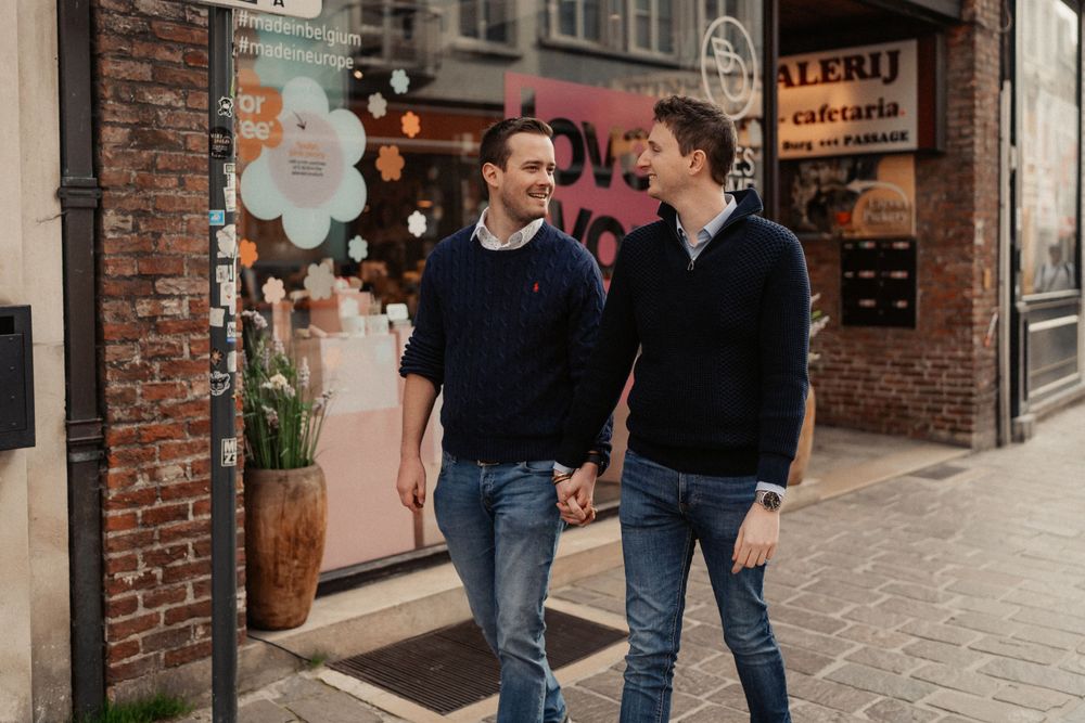 Two people in navy sweaters walking past urban storefronts.