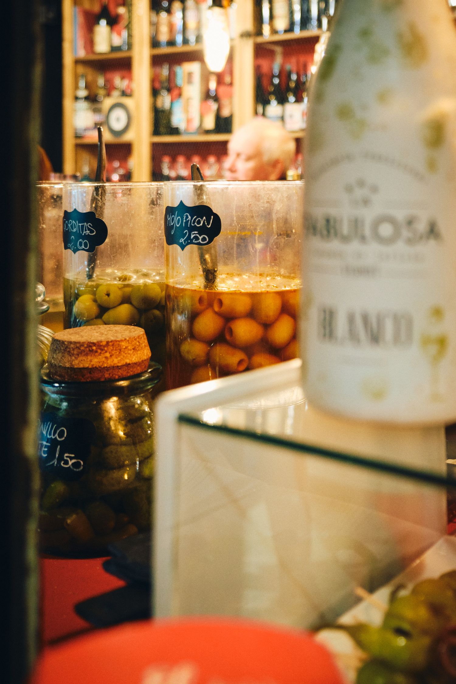 Glass jars filled with colorful pickled vegetables and olives on display at a bar counter.