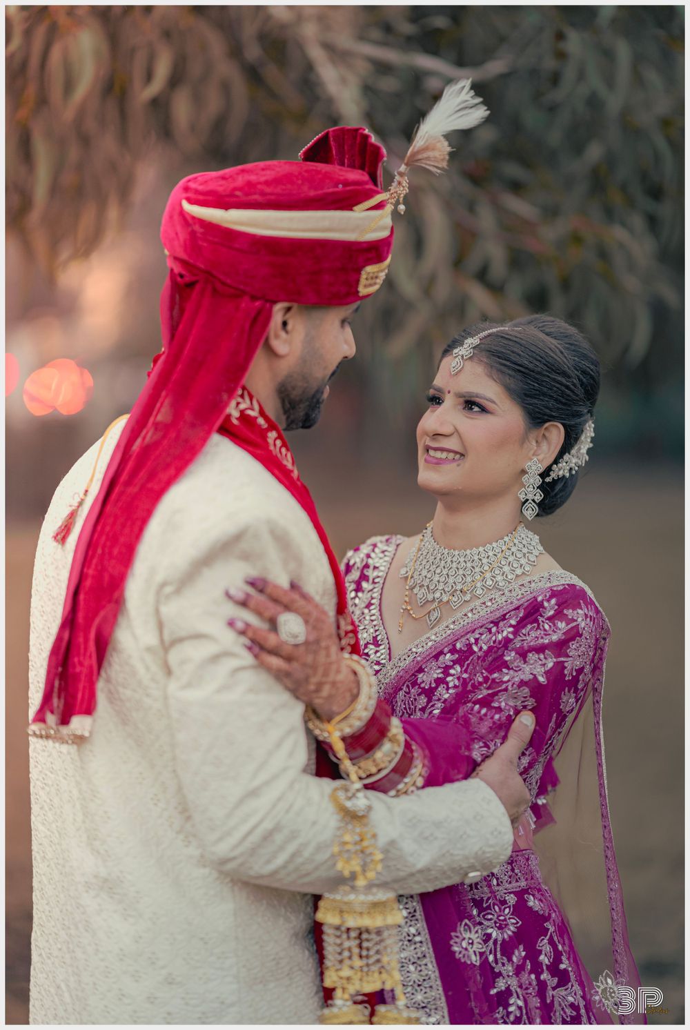 Traditional Indian wedding couple in elegant red and cream outfits pose together.