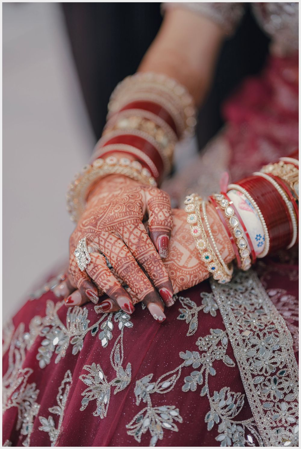 Close-up of henna adorned hands with traditional wedding bangles on embroidered red fabric.