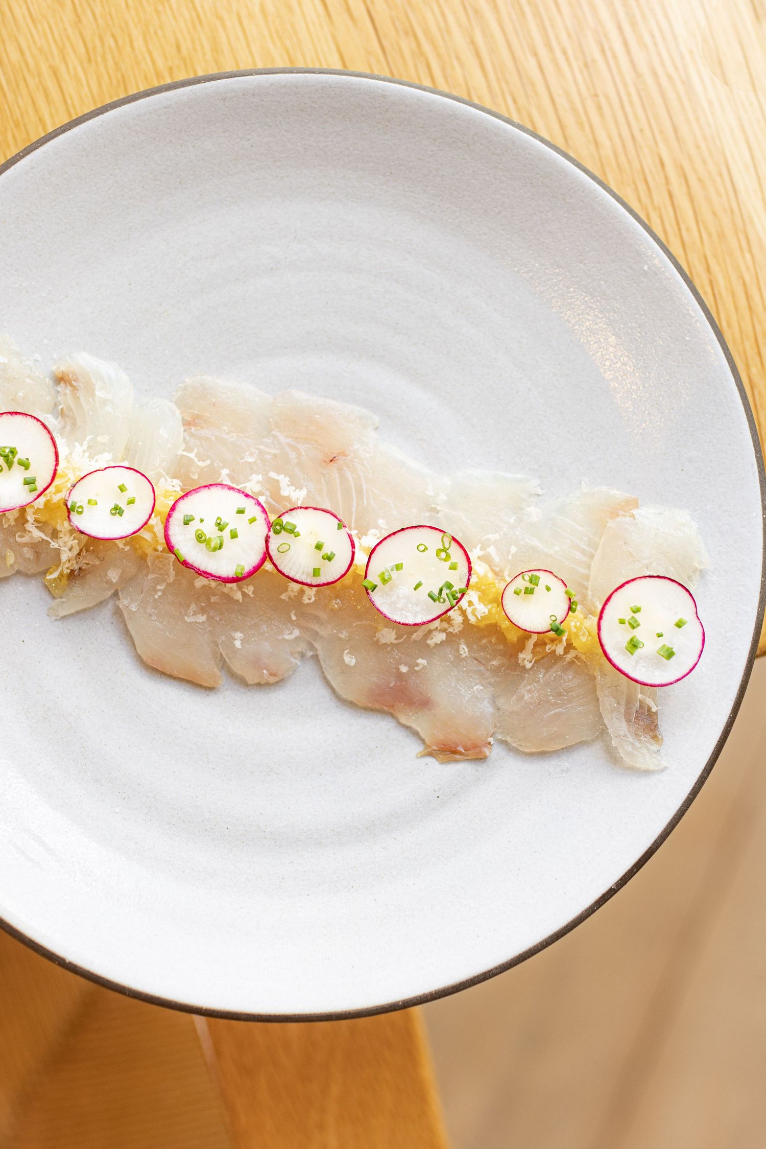Elegant plated sashimi dish with sliced radish and microgreen garnishes on white porcelain.
