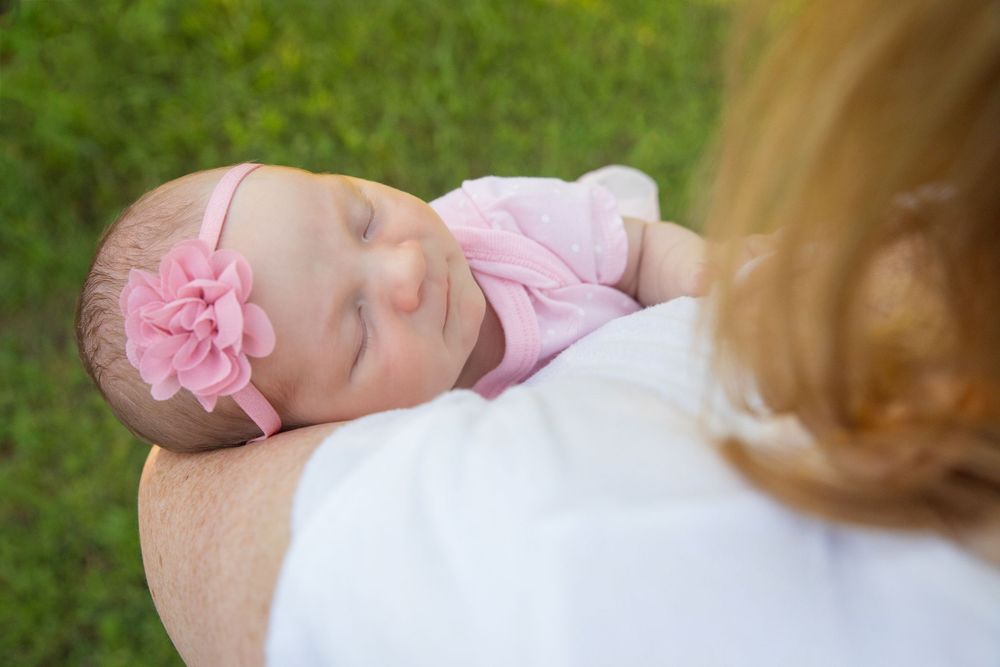 Sleeping baby in pink outfit with floral bow resting outdoors.