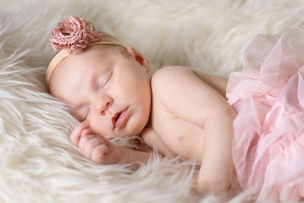 Sleeping baby on white fur with pink floral headband and tulle detail.