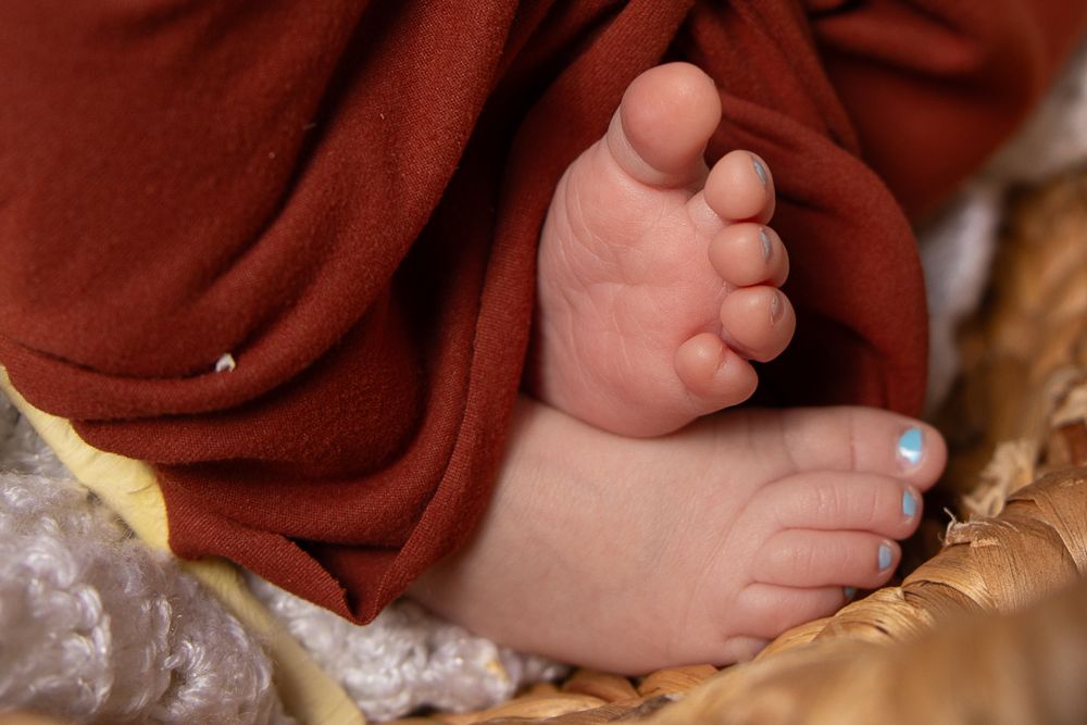 Close-up of tiny baby feet wrapped in rust-colored fabric resting in woven basket.