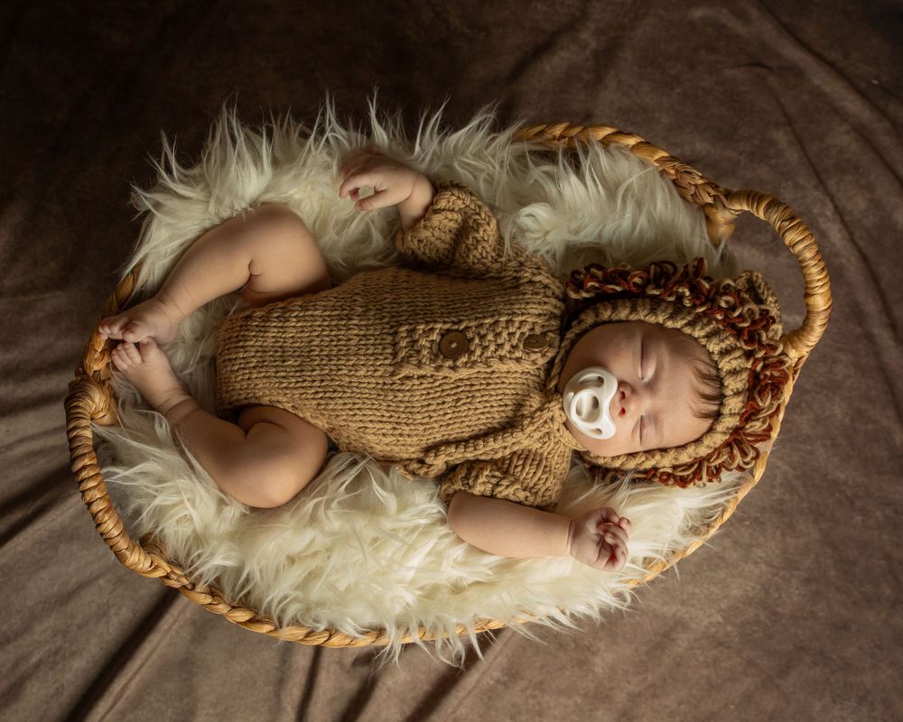Baby in knit outfit resting in wooden basket on fluffy white fur.