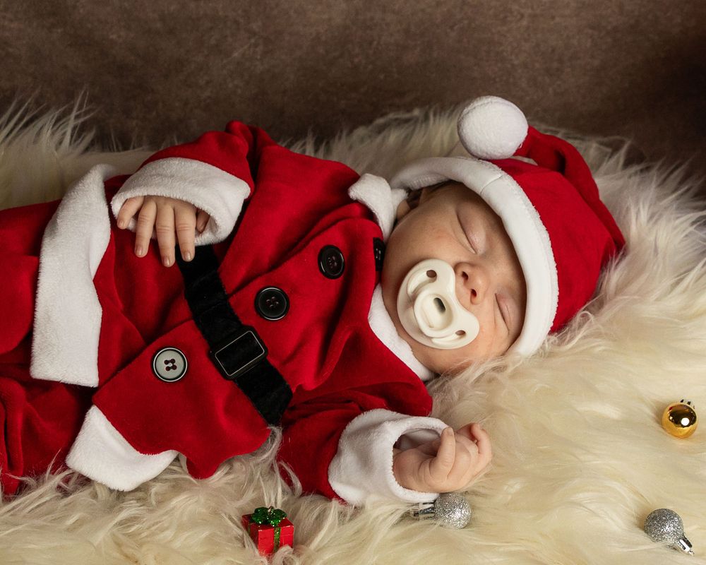 Baby in Santa costume smiling while lying on white furry backdrop.