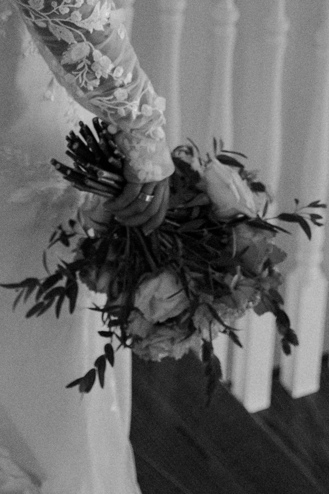 Artistic black and white photograph of flowers and foliage arranged in a vase casting dramatic shadows against curtains.