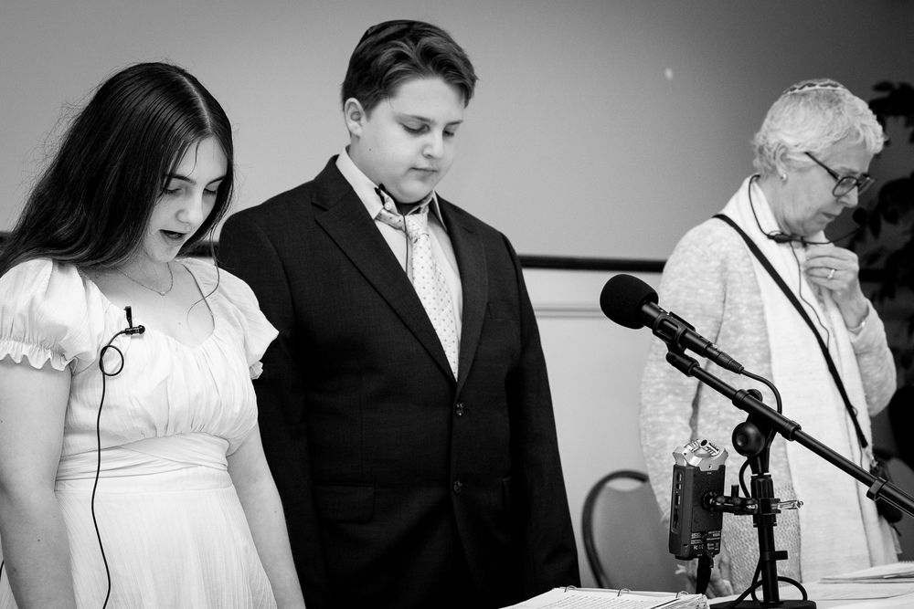 A black and white photograph of three people standing at microphones during a ceremony.