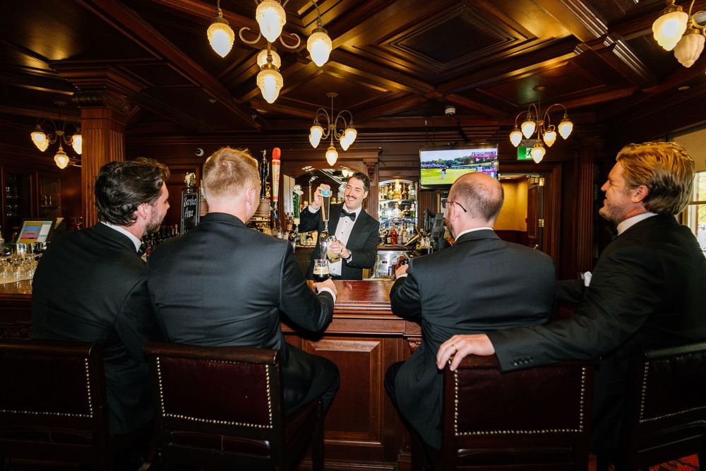 Wedding guests seated at a dimly lit wooden bar with vintage pendant lighting creating an intimate ambiance.