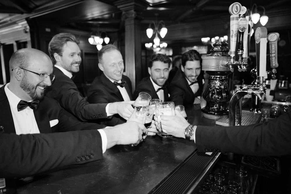 Black and white photo of wedding guests socializing and laughing at a dimly lit bar.