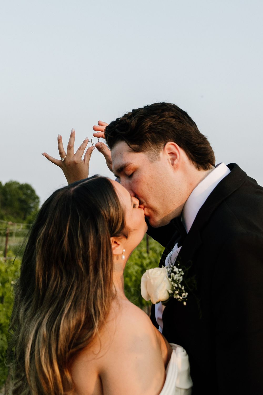 A couple shares an intimate kiss outdoors during their wedding celebration.