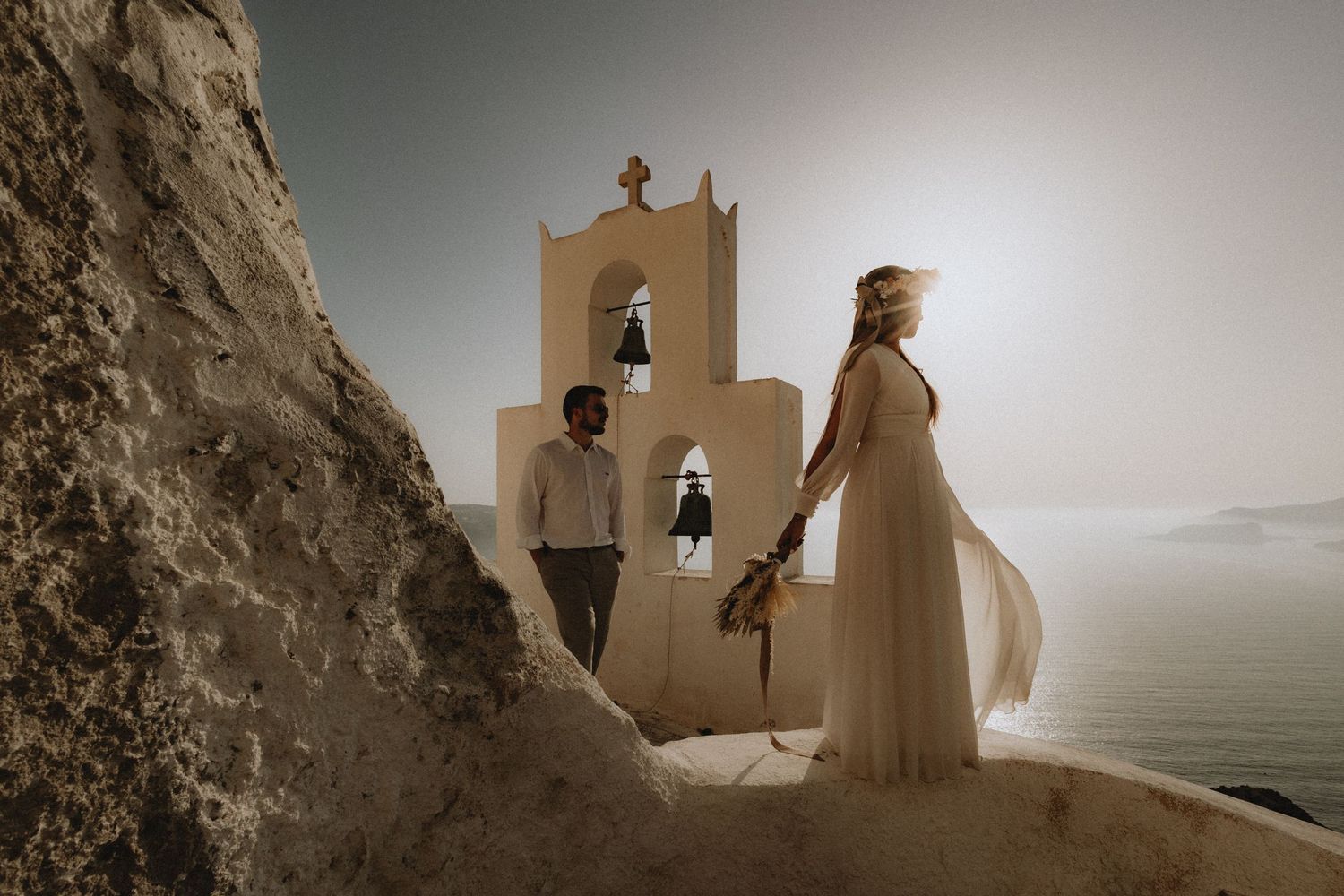 Bride and groom looking at the Aegean sea with a Greek chapel behind them in Santorini.
