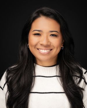 Professional headshot of someone with long dark hair wearing a white striped sweater against a dark background.