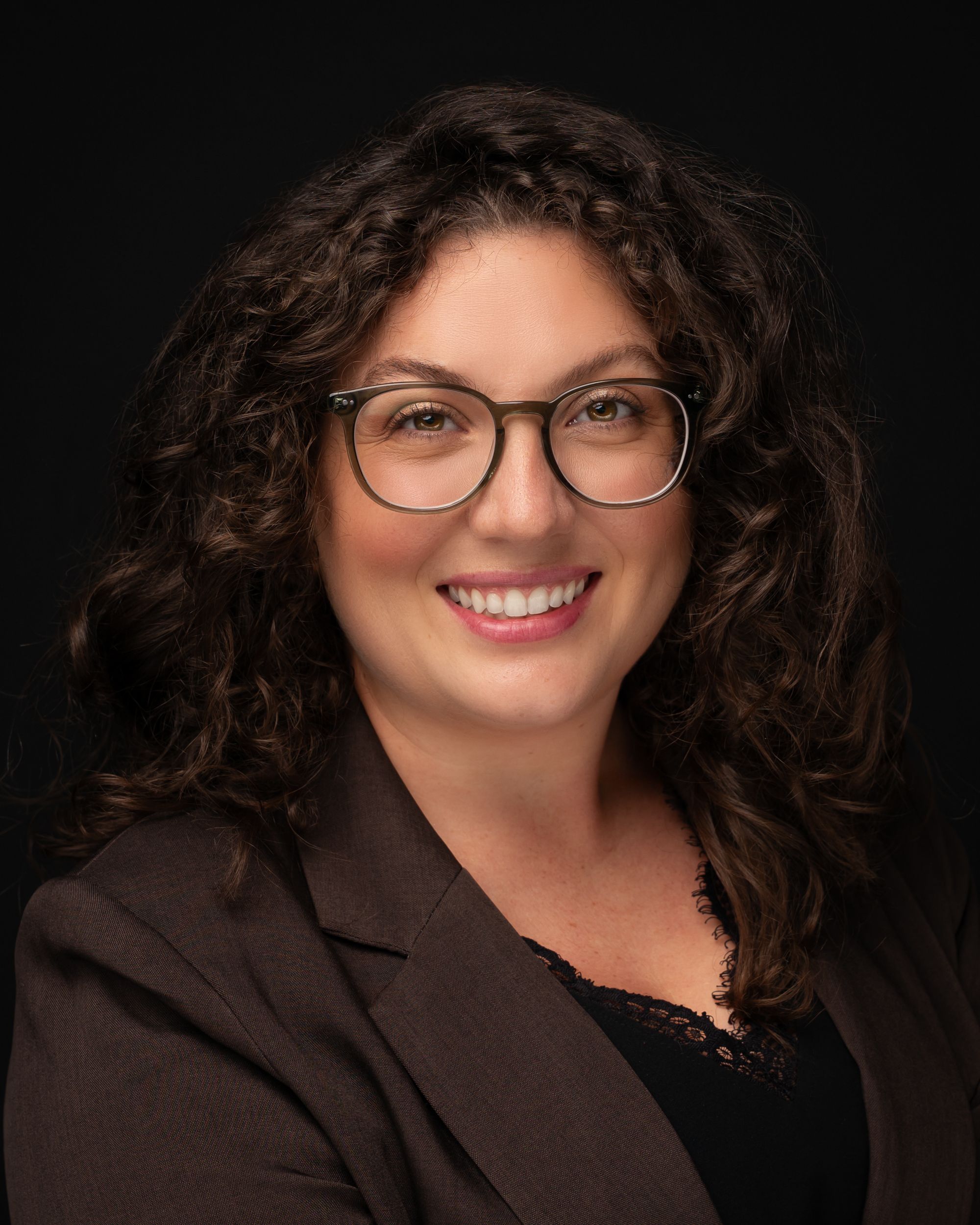 Professional headshot series showing a person with curly hair and glasses against a dark background wearing a brown jacket.