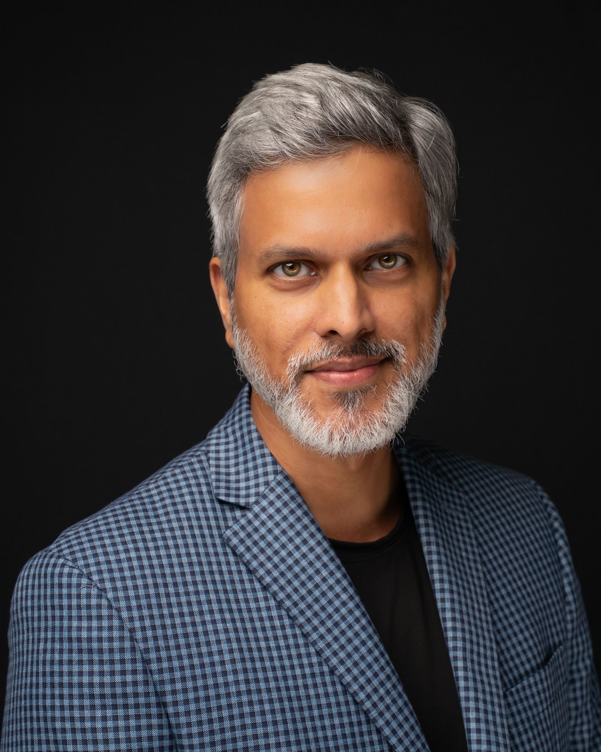 Professional studio portrait of someone wearing a blue checkered shirt against a dark background with dramatic lighting.