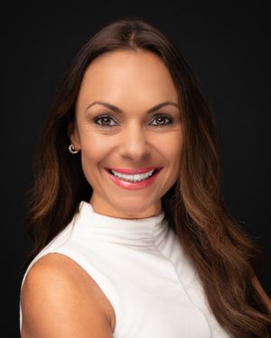Woman in white sleeveless top smiling against black background with dramatic lighting.
