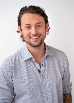 Person in checkered button-down shirt smiling warmly at camera against white backdrop.