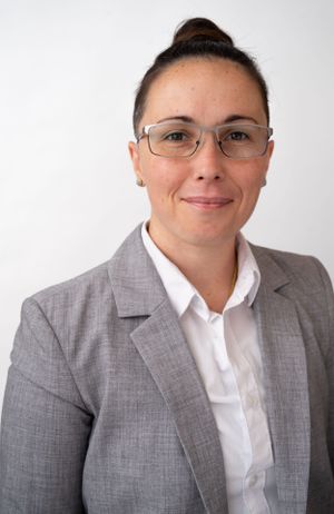 Professional headshot of person wearing glasses, gray blazer and white shirt against white background.