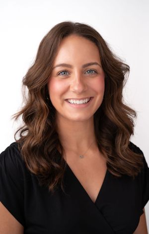 Portrait of person with wavy brown hair wearing black top against white background.