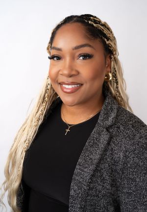 Portrait of person with blonde braids wearing black top and sparkly cardigan against white background.