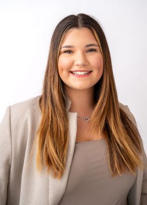 Portrait of person with long brown hair wearing beige blazer against white background.