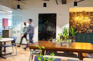 Modern office interior with mixed seating areas, warm lighting, and people in motion.