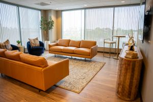 Modern office lounge with tan leather couches and large windows featuring natural light.