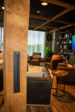 Cozy office lounge area with leather chairs and wooden accents viewed through doorframe.