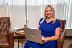Professional working on laptop in modern office space with leather furniture and natural lighting.