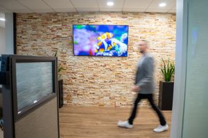 Motion blur of person walking past mounted TV on textured stone wall in modern office hallway.